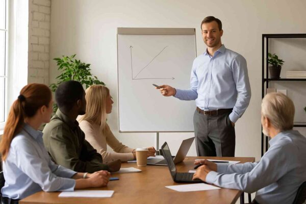 Employees attending a workplace training session with a presenter explaining on a whiteboard in a bright modern office.