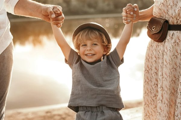 Parents holding hands of smiling child - Parent-child relationships